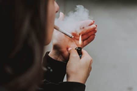 Sachets de nicotine : bannir ou contrôler ? Tout comprendre sur le débat en cours Close-up of a woman lighting a cigarette outdoors with a lighter, smoke visible.
