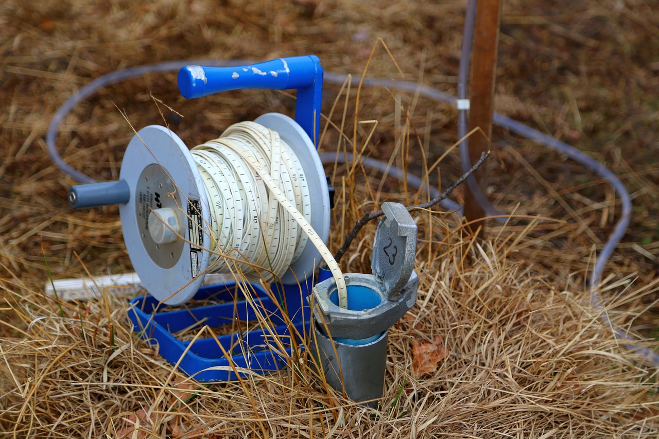 Dévidoir bleu et blanc d'une sonde de mesure posé sur de la paille, avec un seau gris à côté.